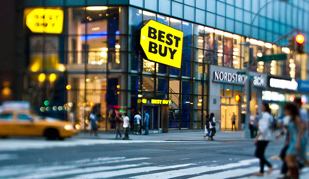 Pedestrians pass in front of a Best Buy Co. store in this photo taken with a tilt-shift lens in New York, U.S., on Sunday, June 12, 2011. Best Buy Co., the world's largest consumer electronics retailer, is scheduled to announce quarterly earnings on June 14 before the opening of U.S. financial markets. Photographer: Chris Goodney/Bloomberg via Getty Images